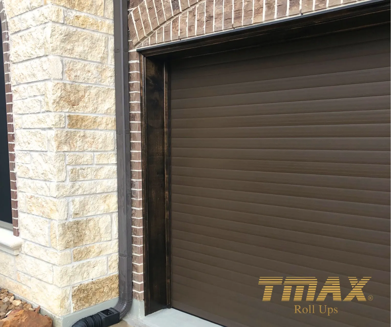 Close view of a brown TMAX roll-up garage door on a brick and stone home
