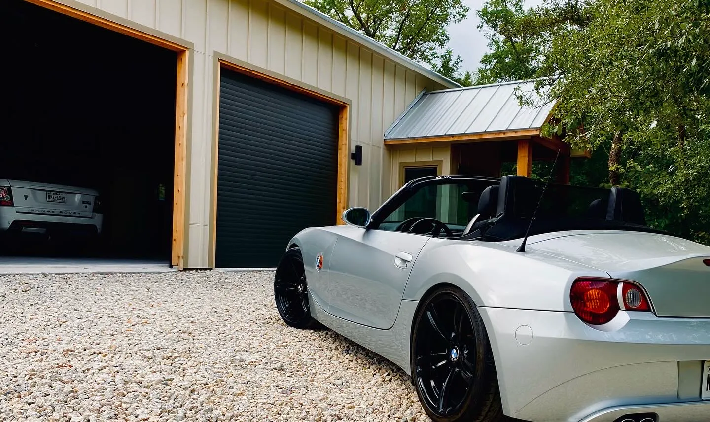 Black TMAX roll-up garage doors on a country garage with a white BMW roadster