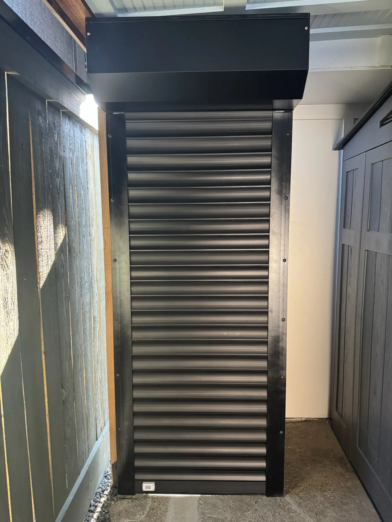 Compact black roll-down shutter installed beneath an awning